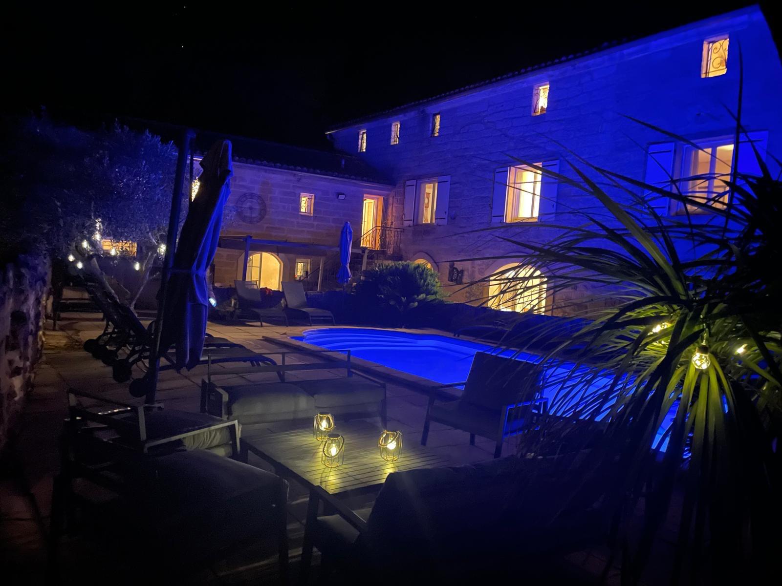 La piscine et la façade du mas illuminées à la nuit tombée